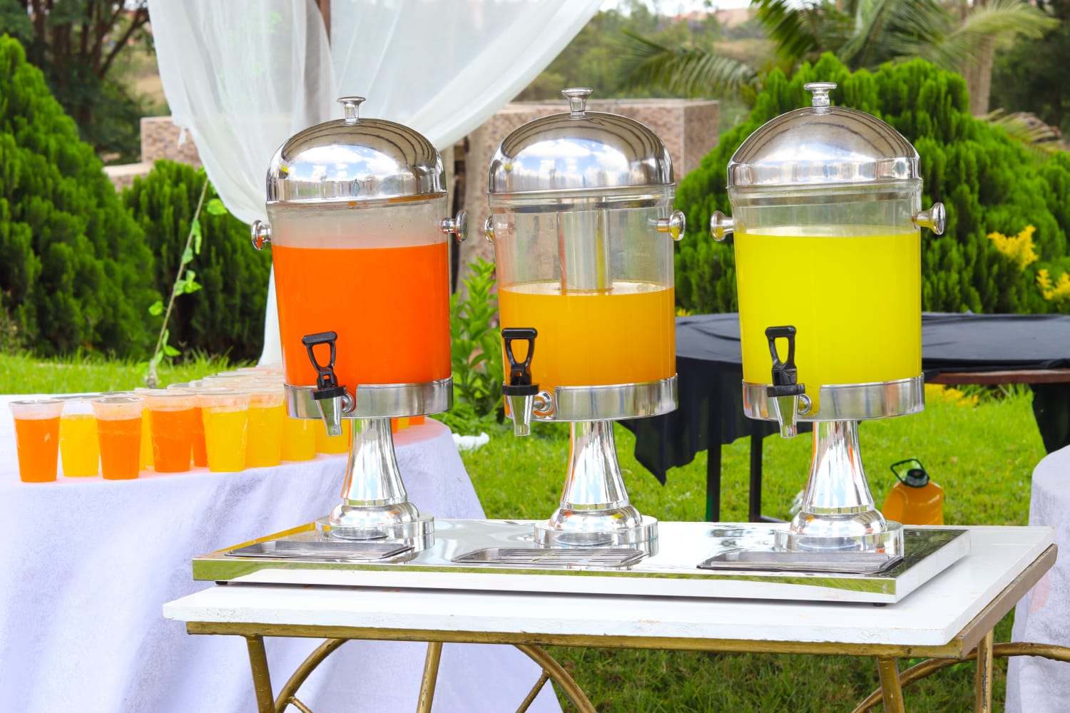 Three juice dispensers at an outdoor refreshment station